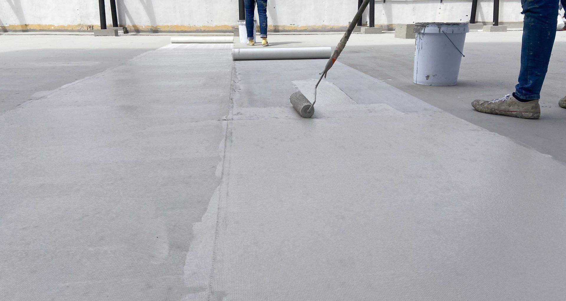 Workers smoothing wet concrete with a long-handled tool on a construction site