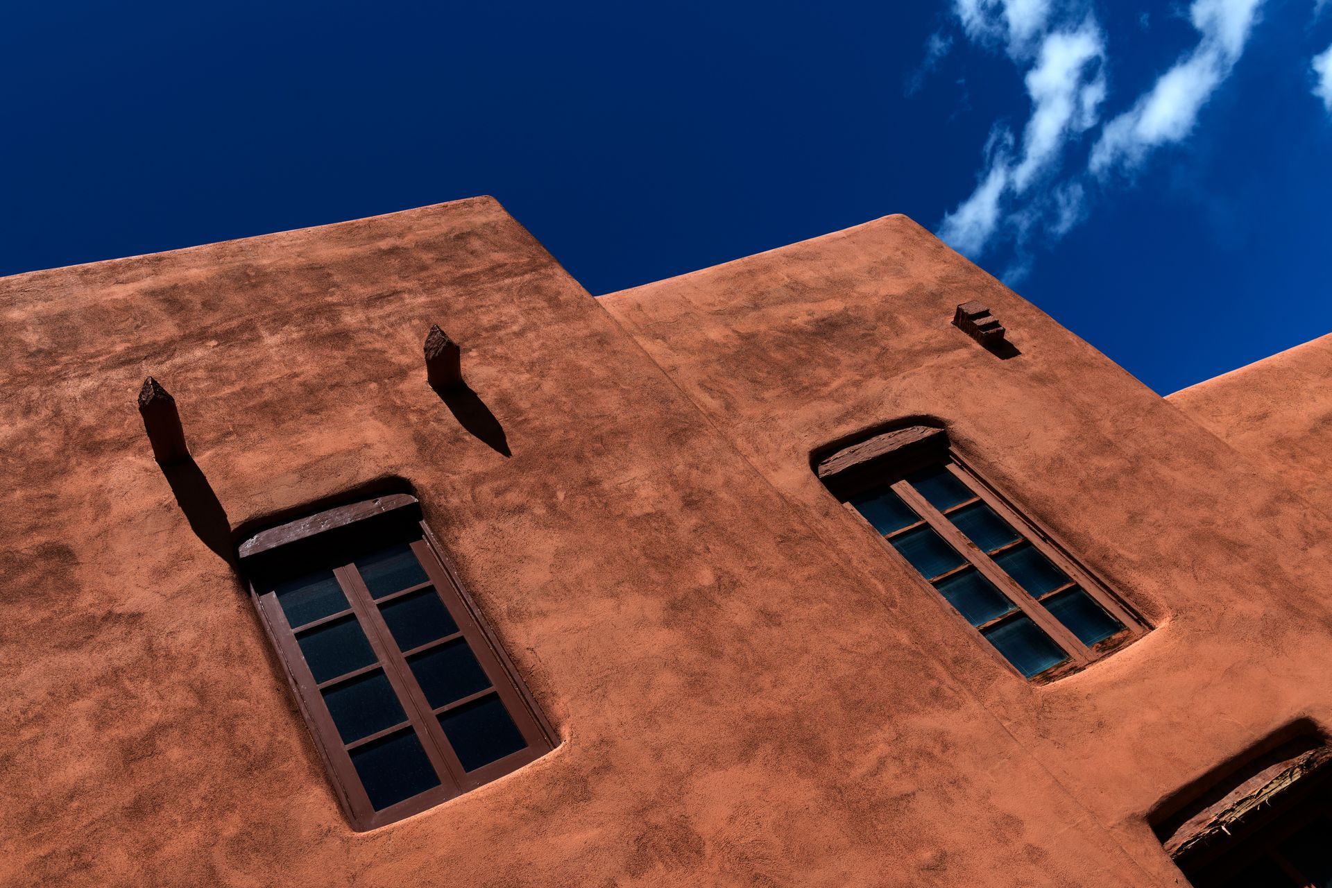 Sunlit adobe building facade with blue-trimmed windows against a deep blue sky