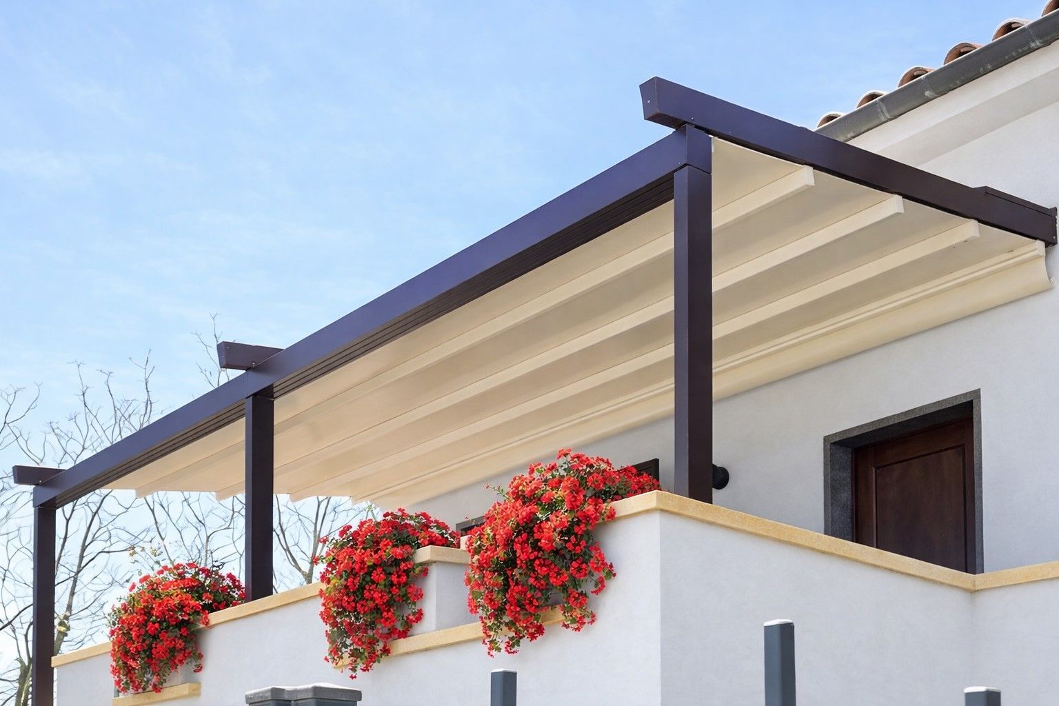 Patio di una casa bianca con travi scure e piante fiorite rosse sul balcone.