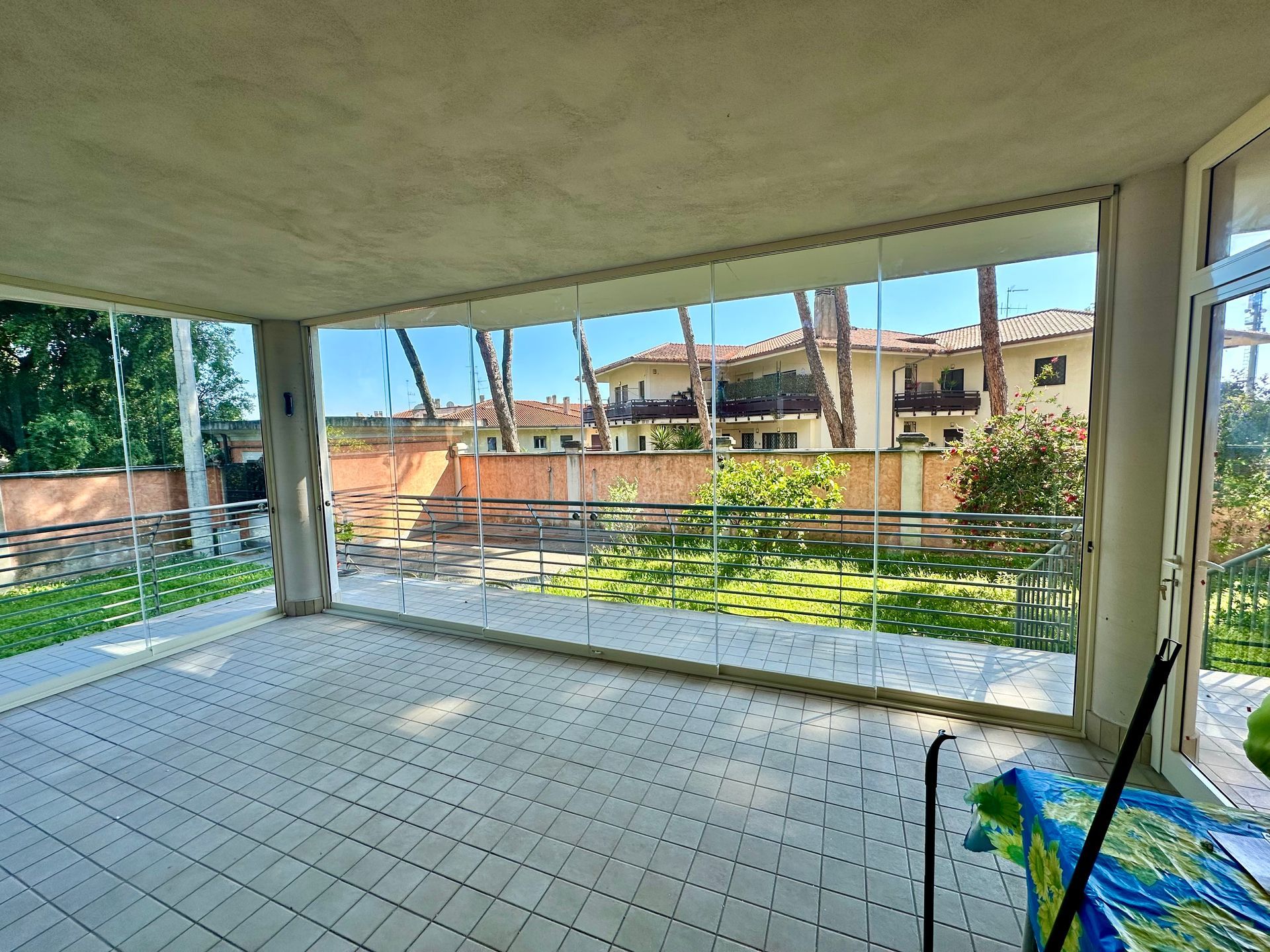 Patio coperto vuoto con pavimento piastrellato e ringhiera in vetro che si affaccia su un cortile residenziale.