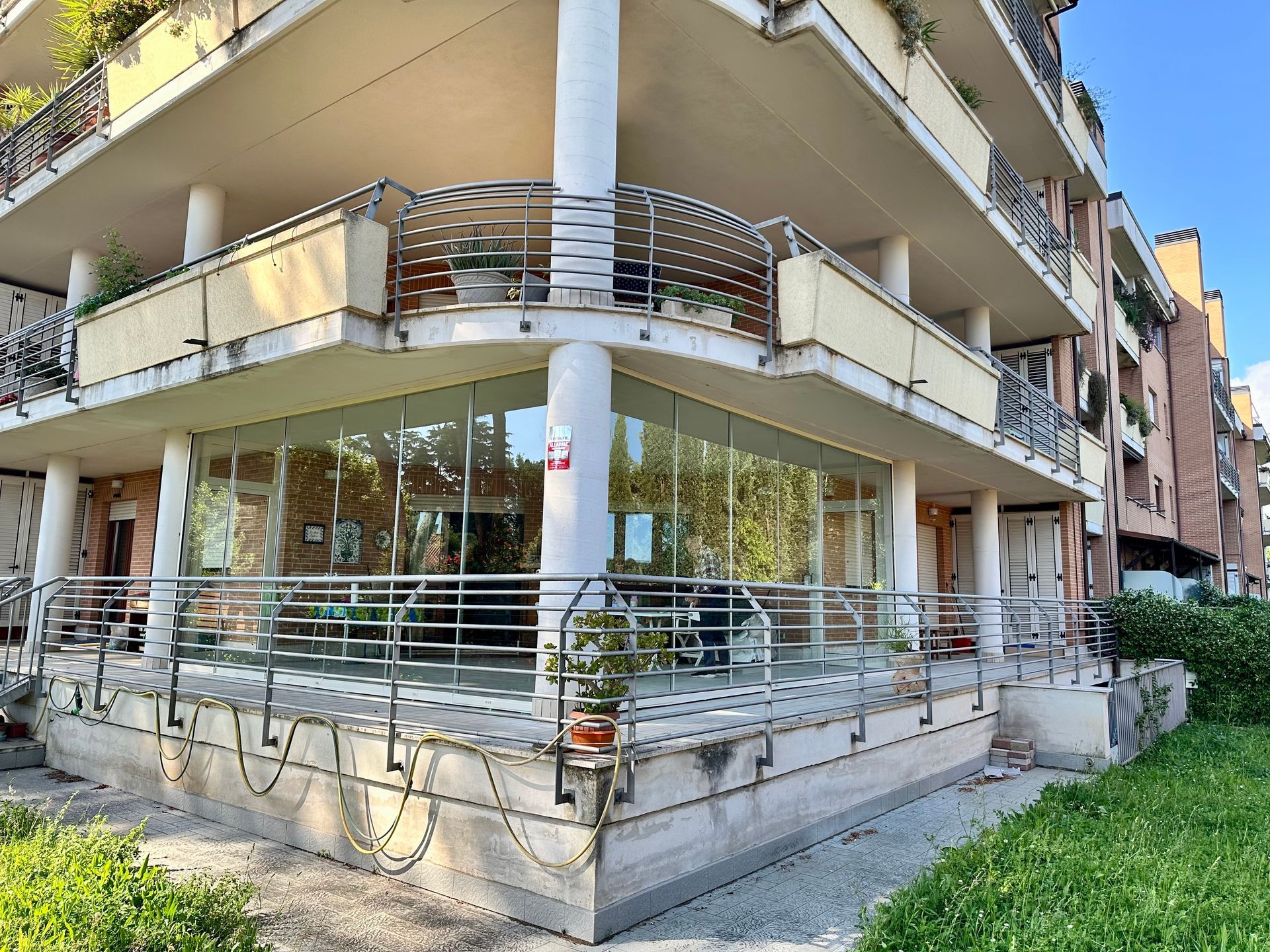 Moderno condominio angolare con balconi, vetrine e rampa metallica su una strada soleggiata