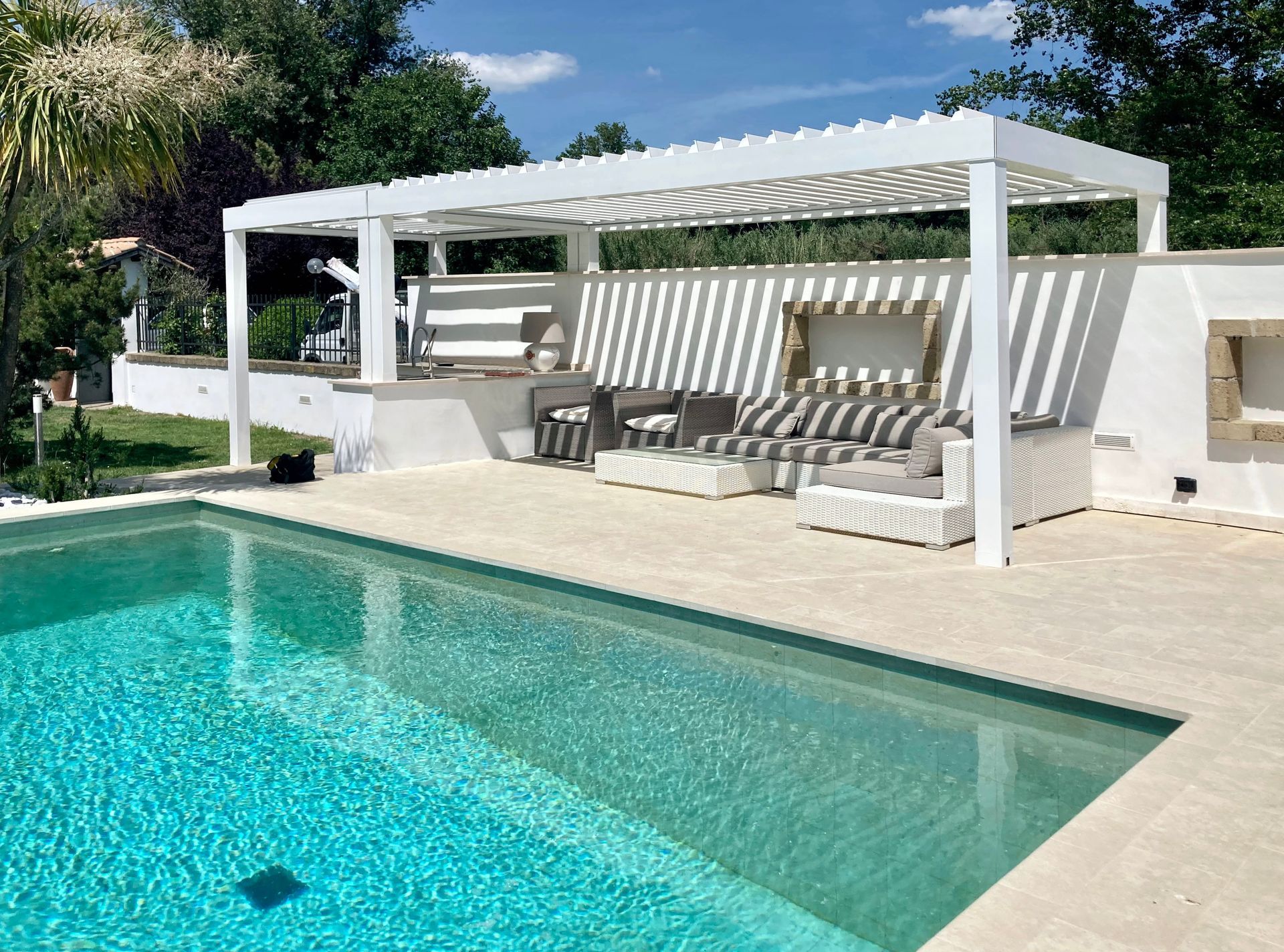 Lussuoso patio a bordo piscina con pergola bianca, lettini e piscina turchese sotto un cielo limpido