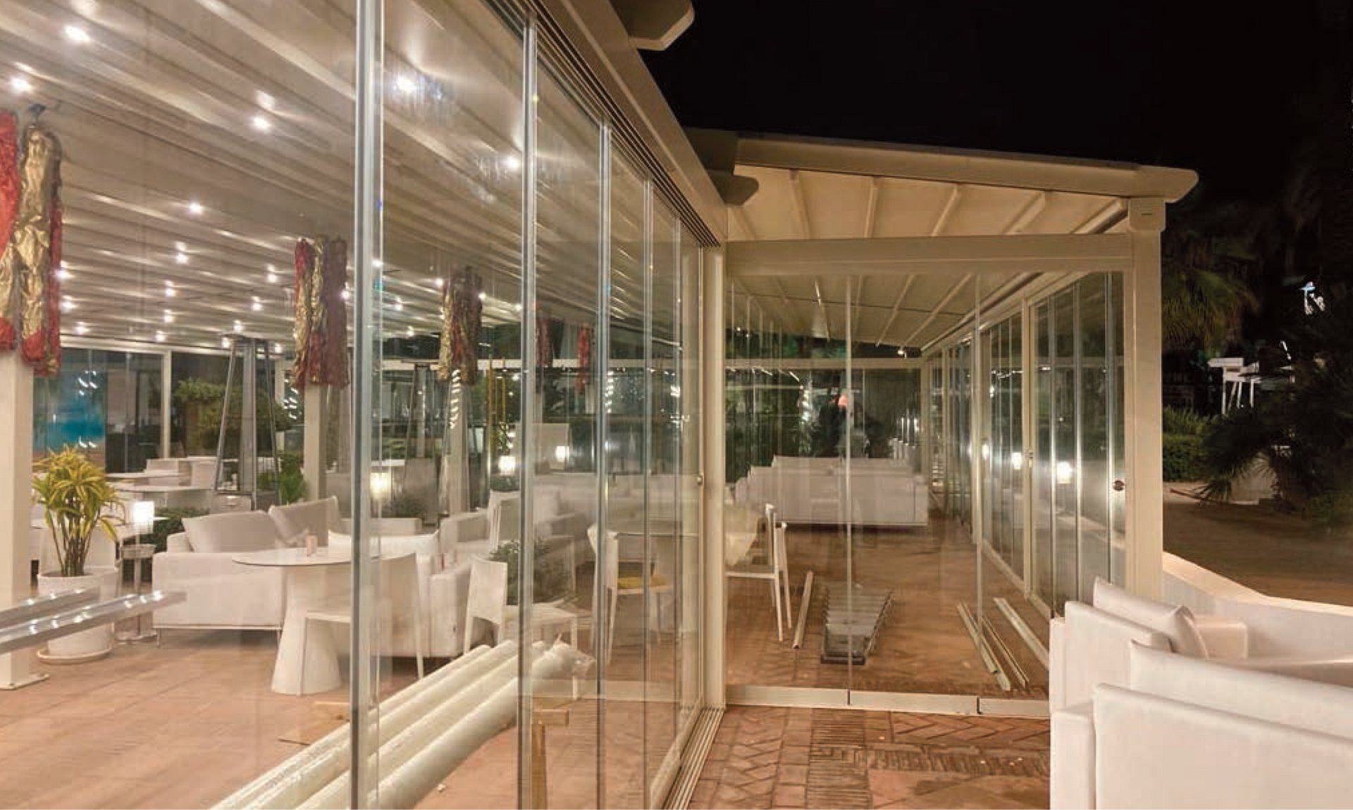 Patio moderno con pareti in vetro, sedie blu e piante in vaso su una soleggiata terrazza di casa.