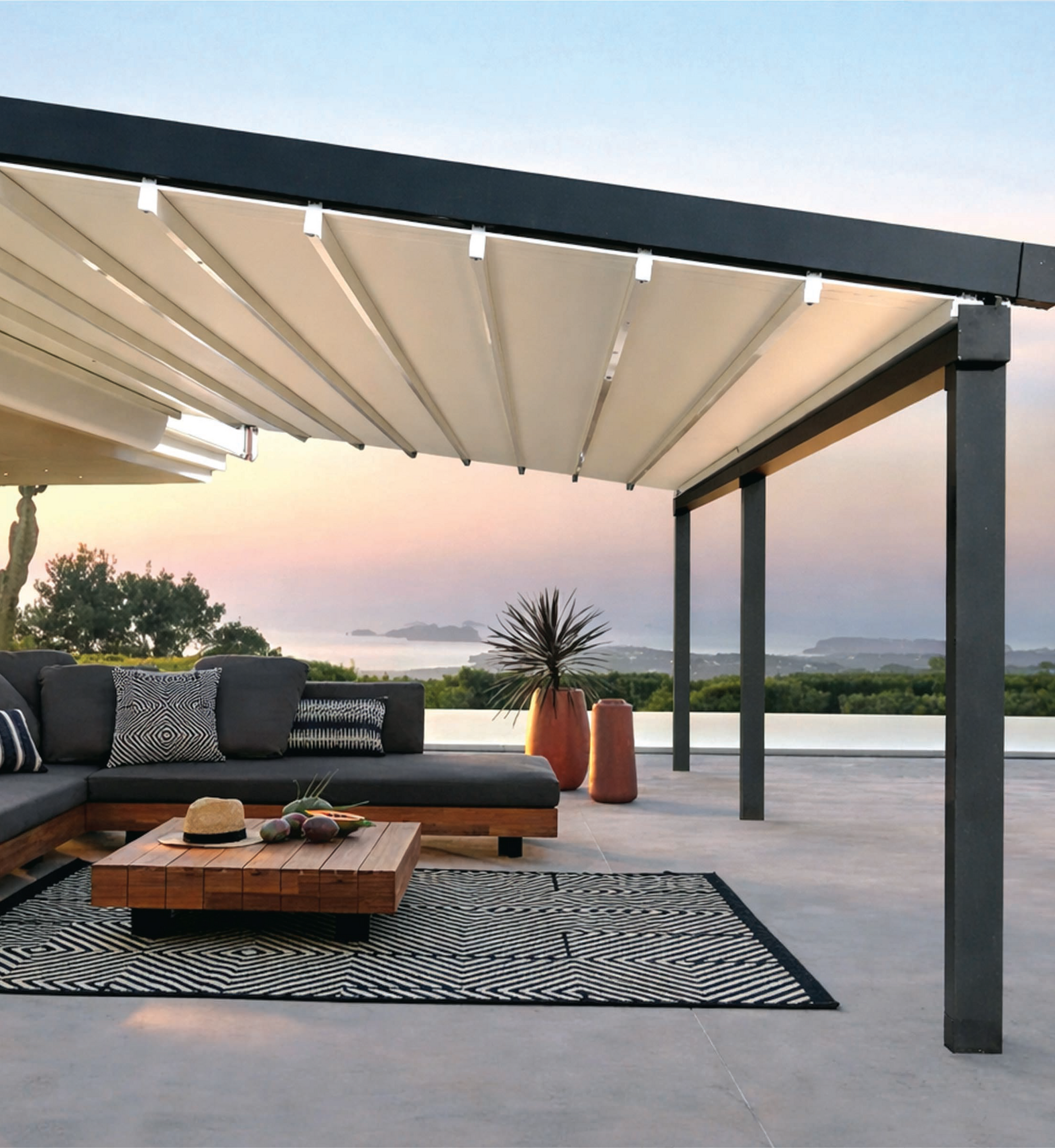 Moderno patio esterno con divano componibile, tavolino da caffè e tappeto a righe sotto un pergolato al tramonto.