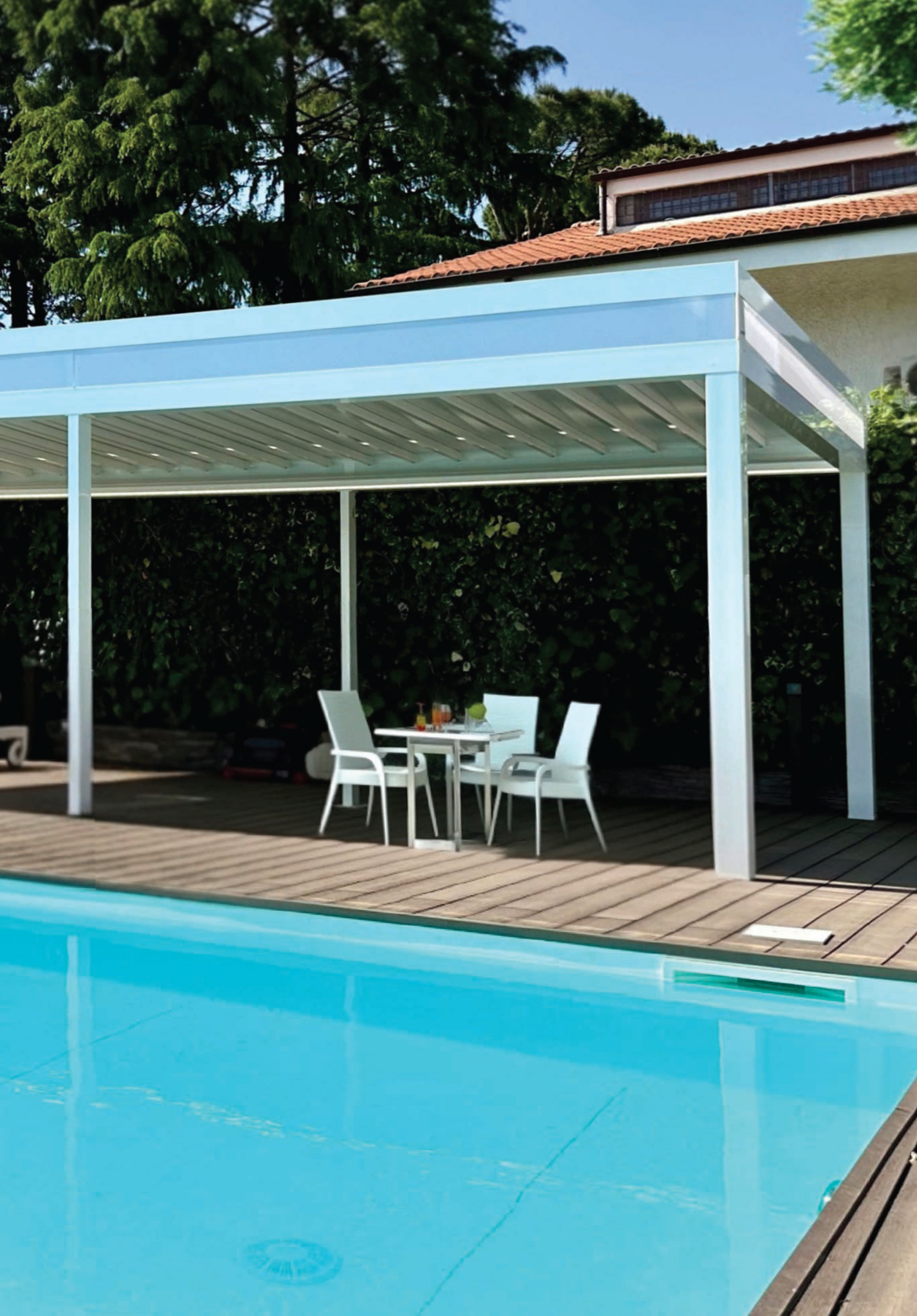 Patio a bordo piscina con pergola bianca, tavolo e sedie accanto a una piscina turchese.