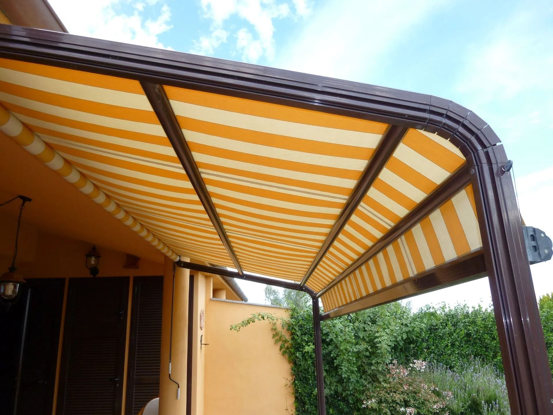 Tenda da sole retrattile a strisce gialle che si estende su un patio contro un cielo azzurro