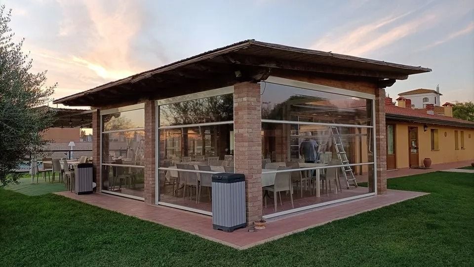 Padiglione da caffè all'aperto con pareti in vetro, colonne in mattoni e prato verde al tramonto.