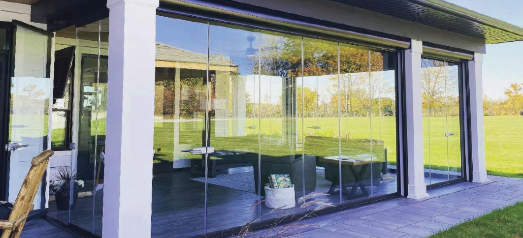 Modern patio with glass walls, curtains, table and chairs, overlooking an outdoor grassy area.