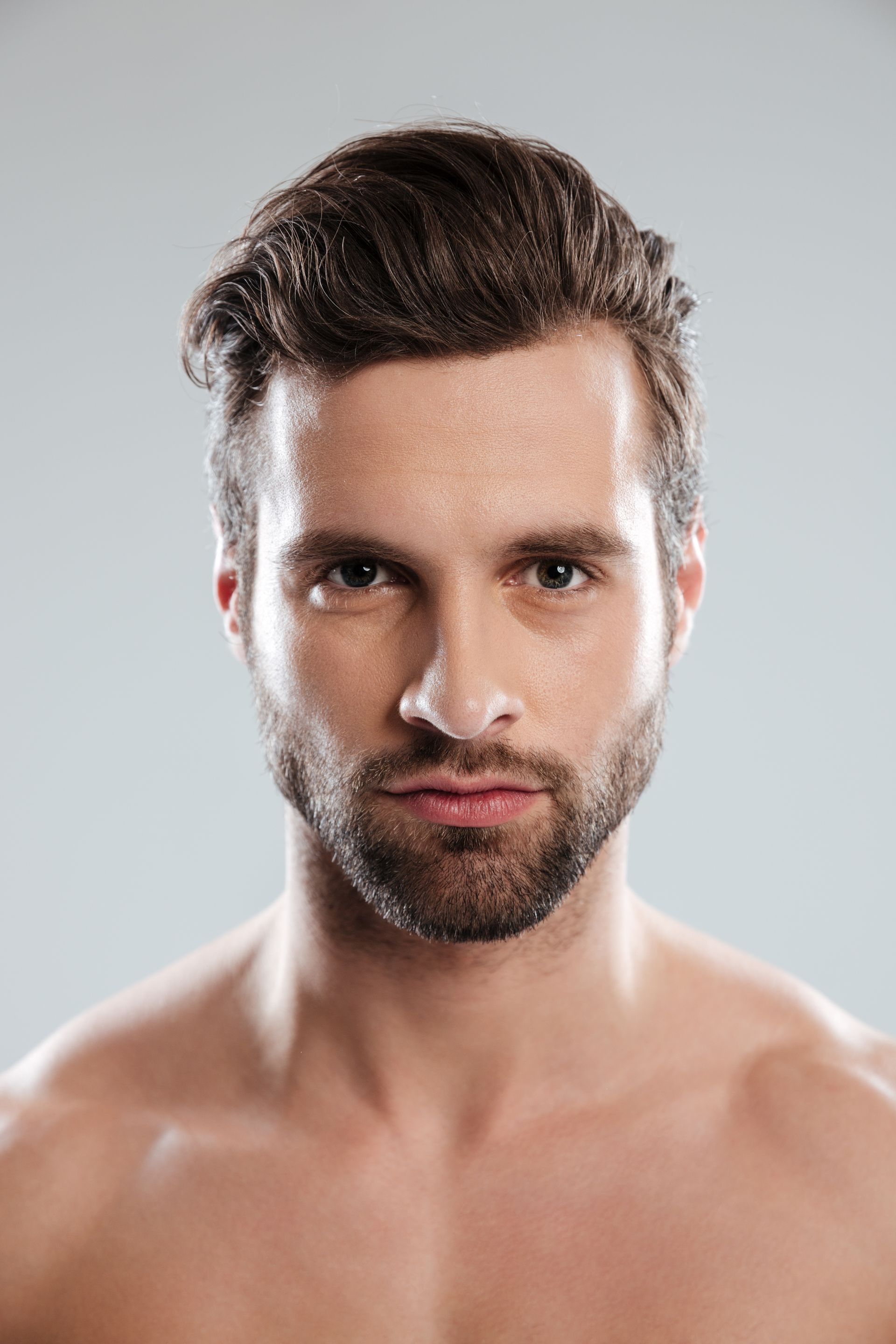 Un hombre sin camisa y con barba mira a la cámara.