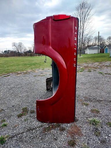 A red truck bed is sitting on top of a gravel road in a field.