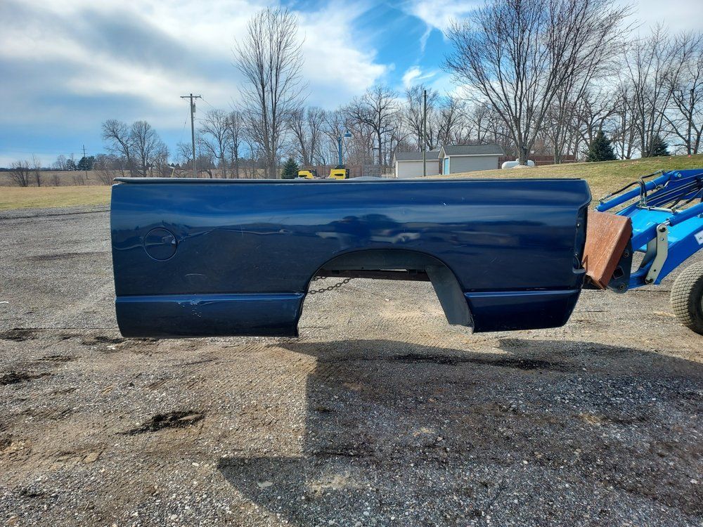 A blue truck bed is sitting on top of a gravel road.