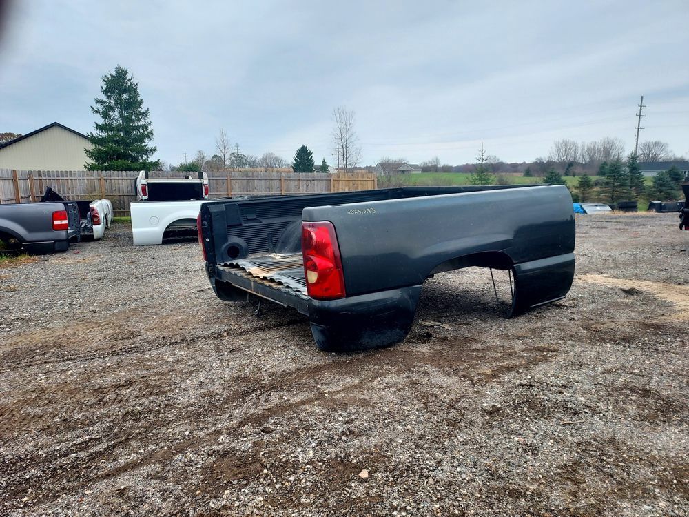 A black truck bed is sitting in a gravel lot.