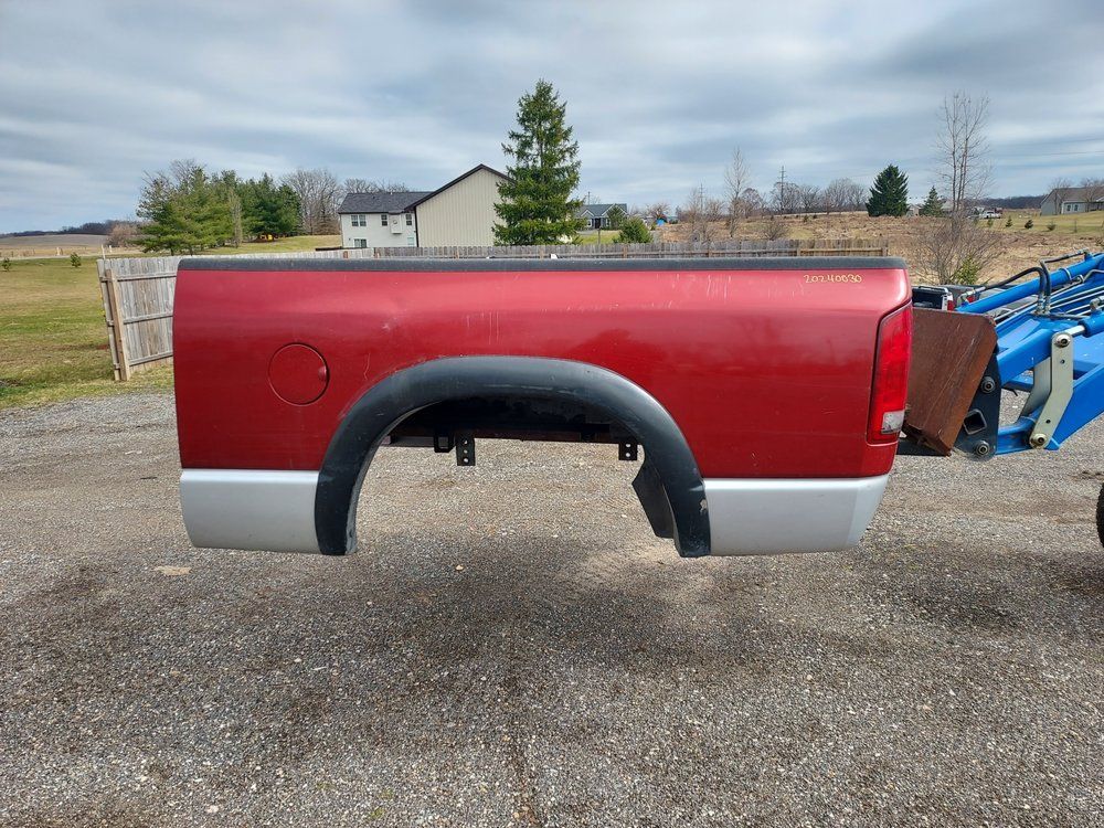 A red truck bed is sitting on the ground next to a blue tractor.