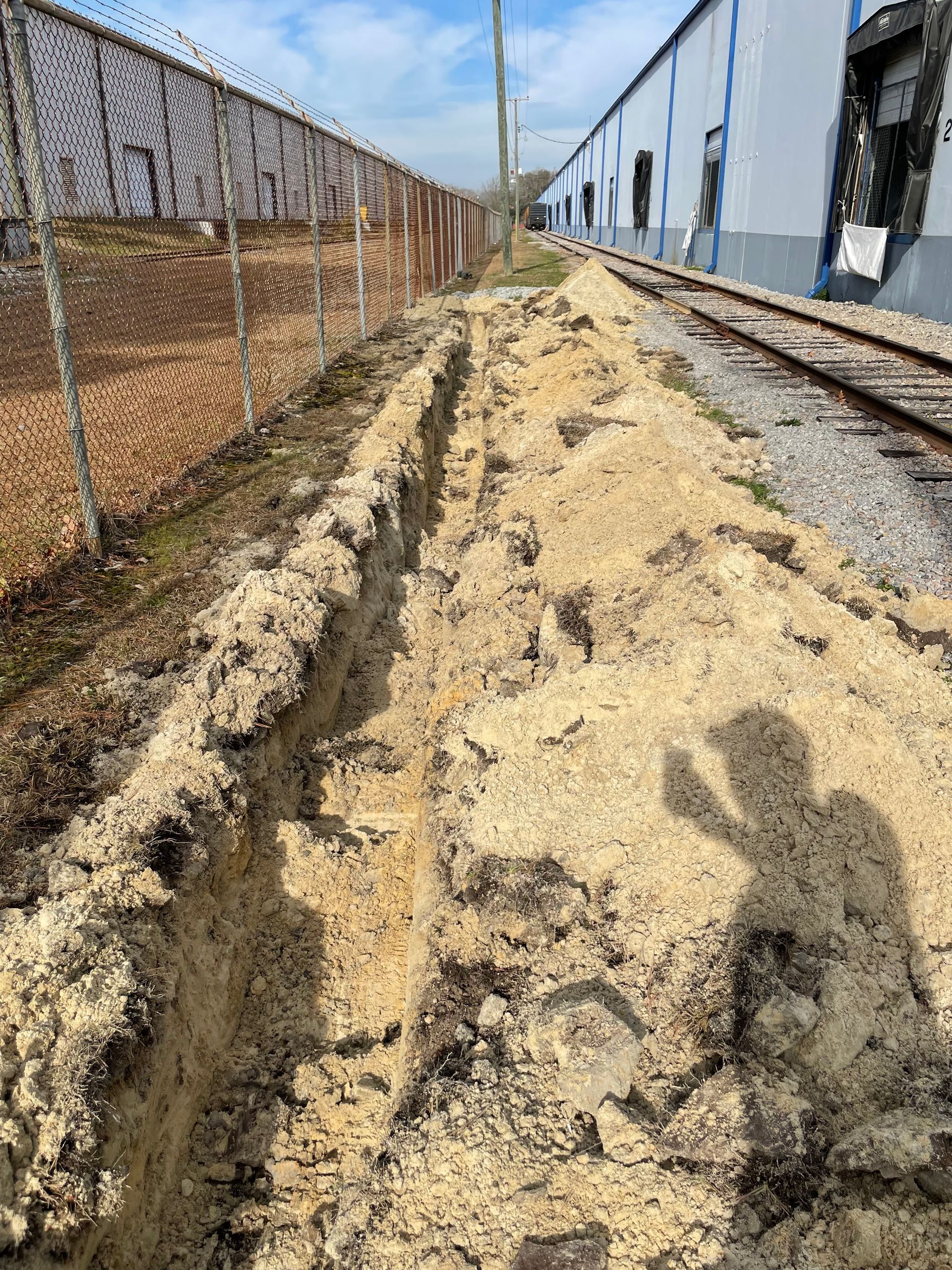 A shadow of a person is cast on a pile of dirt next to train tracks.