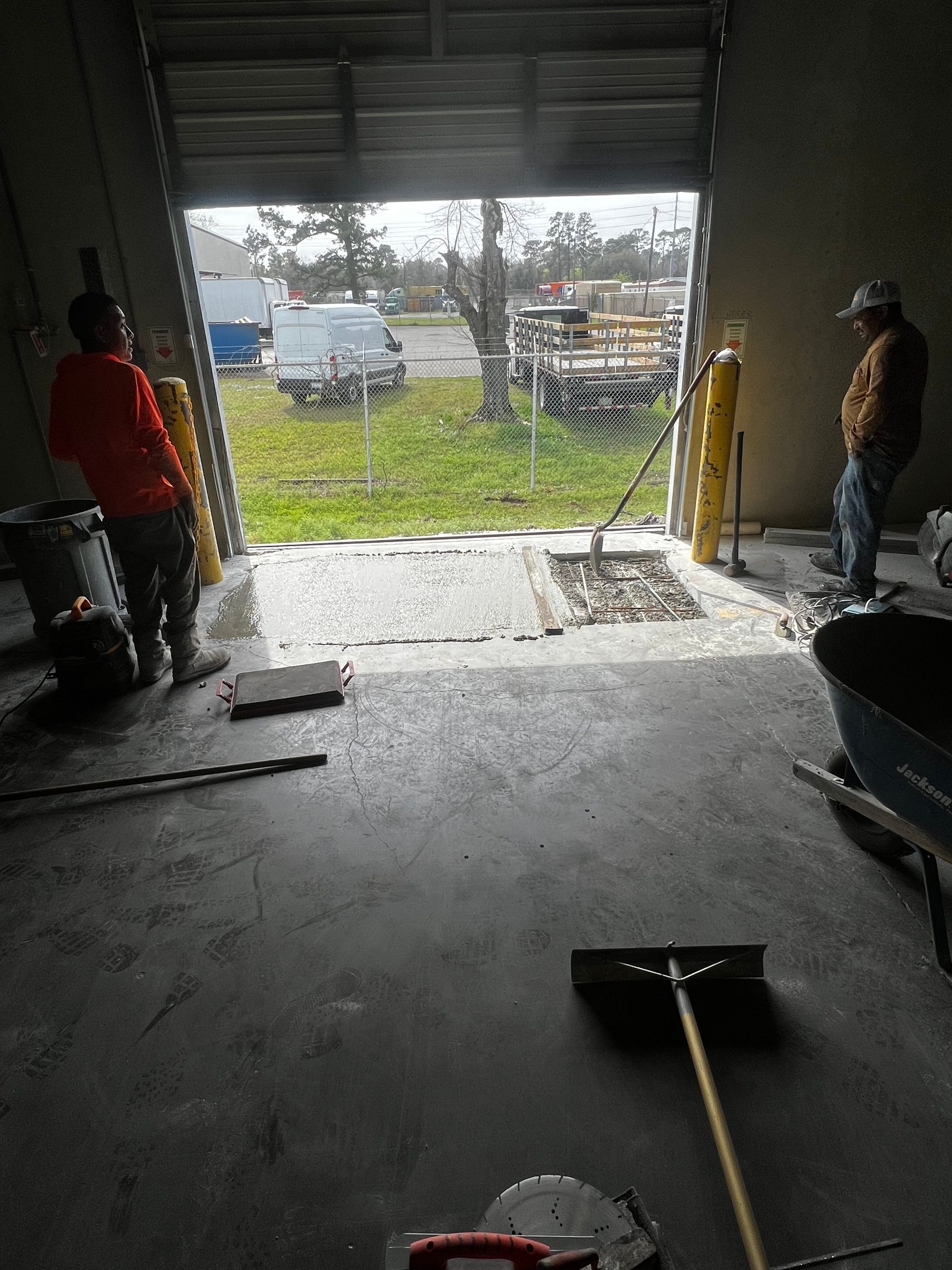 Two men are working in a garage with a broom and wheelbarrow