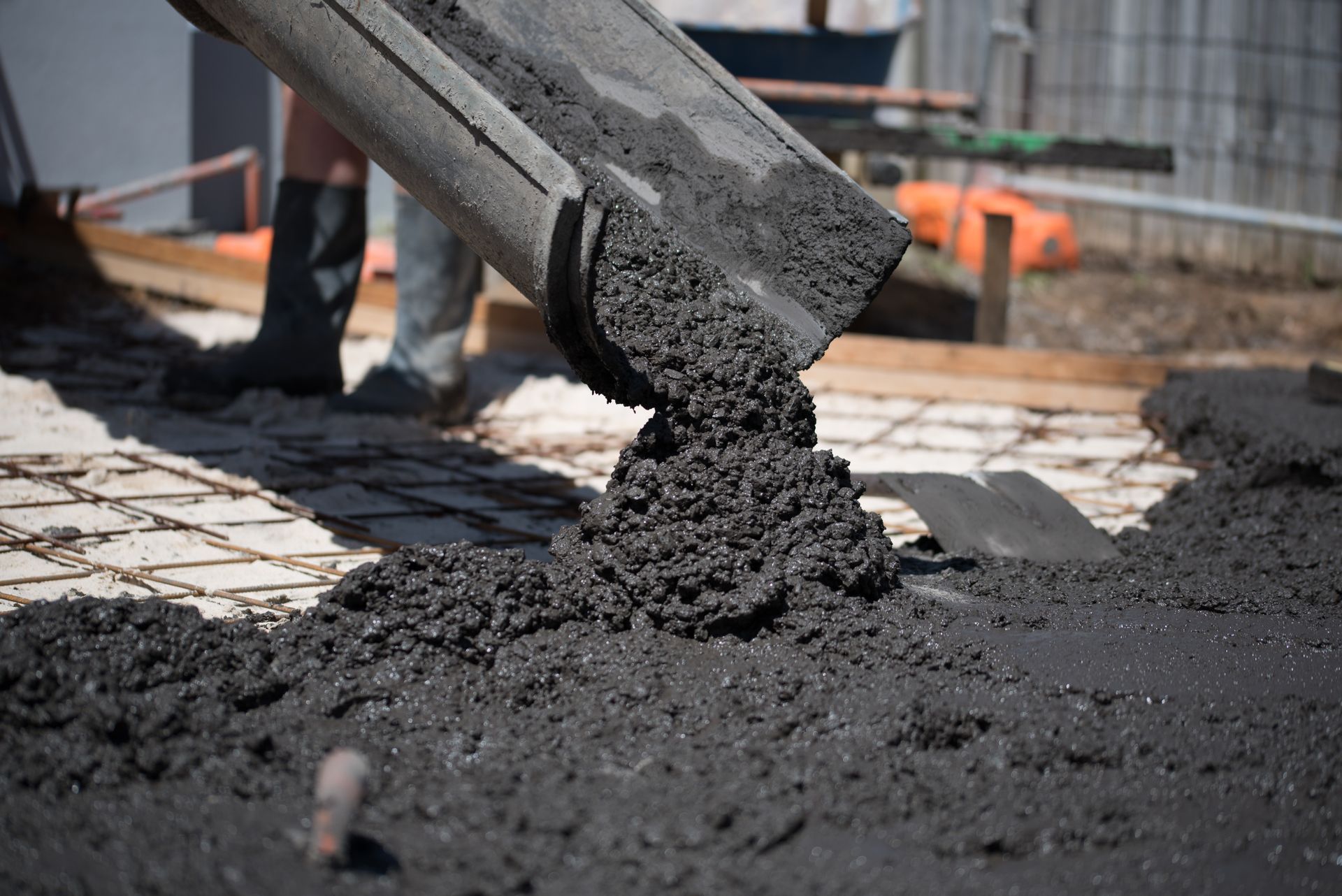 Wet concrete being poured from chute over rebar at construction site.