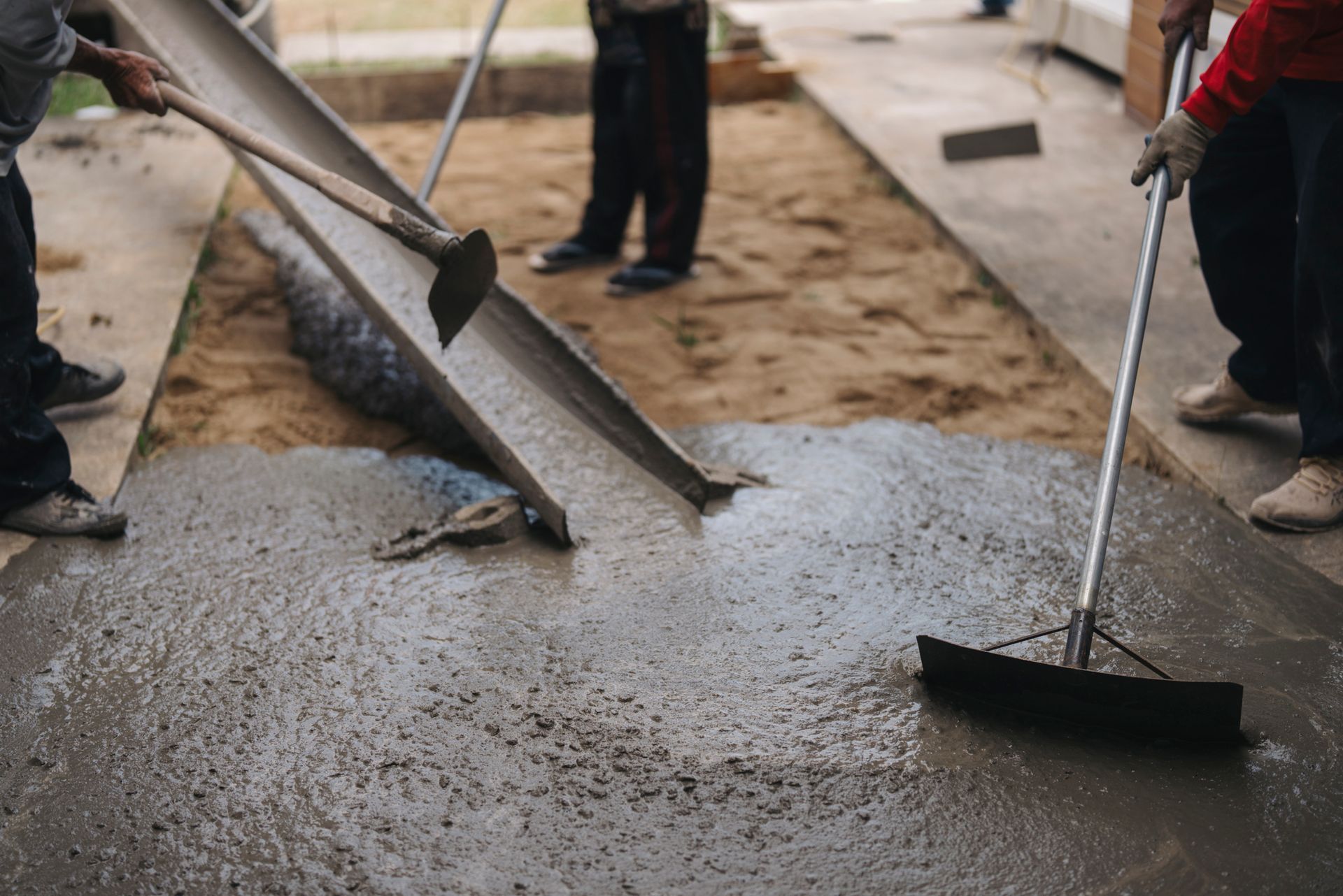 Workers leveling freshly poured concrete from a chute at a construction site.