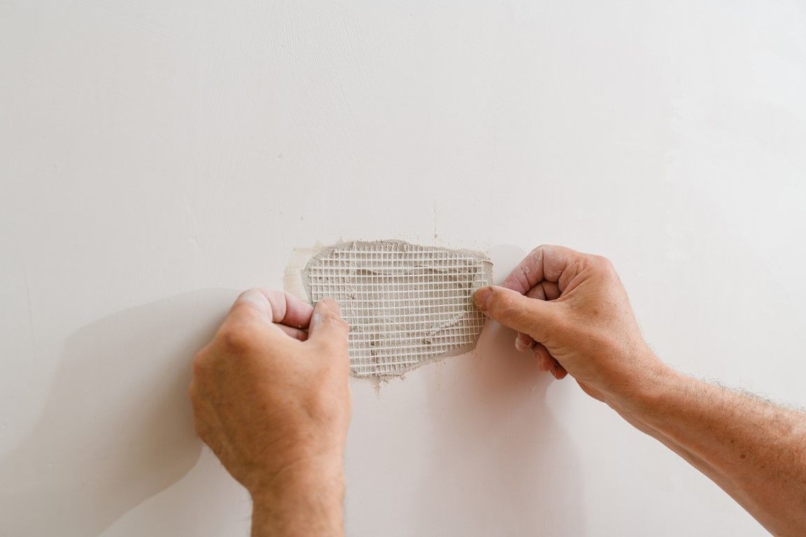 Hands applying mesh tape to a hole in a white wall