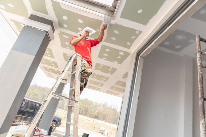 Worker in a red shirt standing on a ladder, installing ceiling panels in a building interior