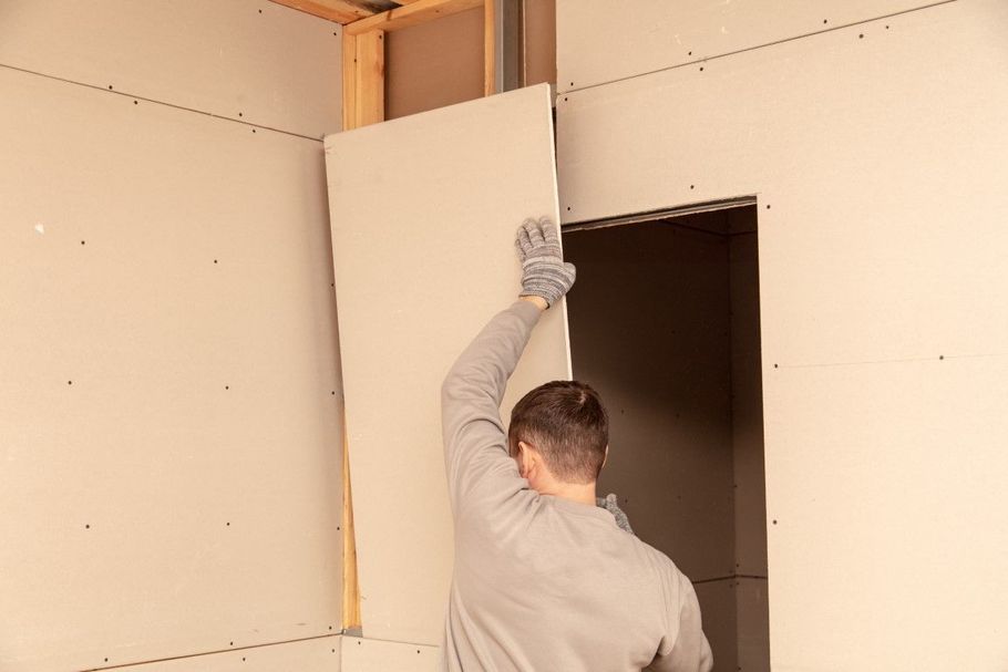 Worker installing a drywall panel in an unfinished room.
