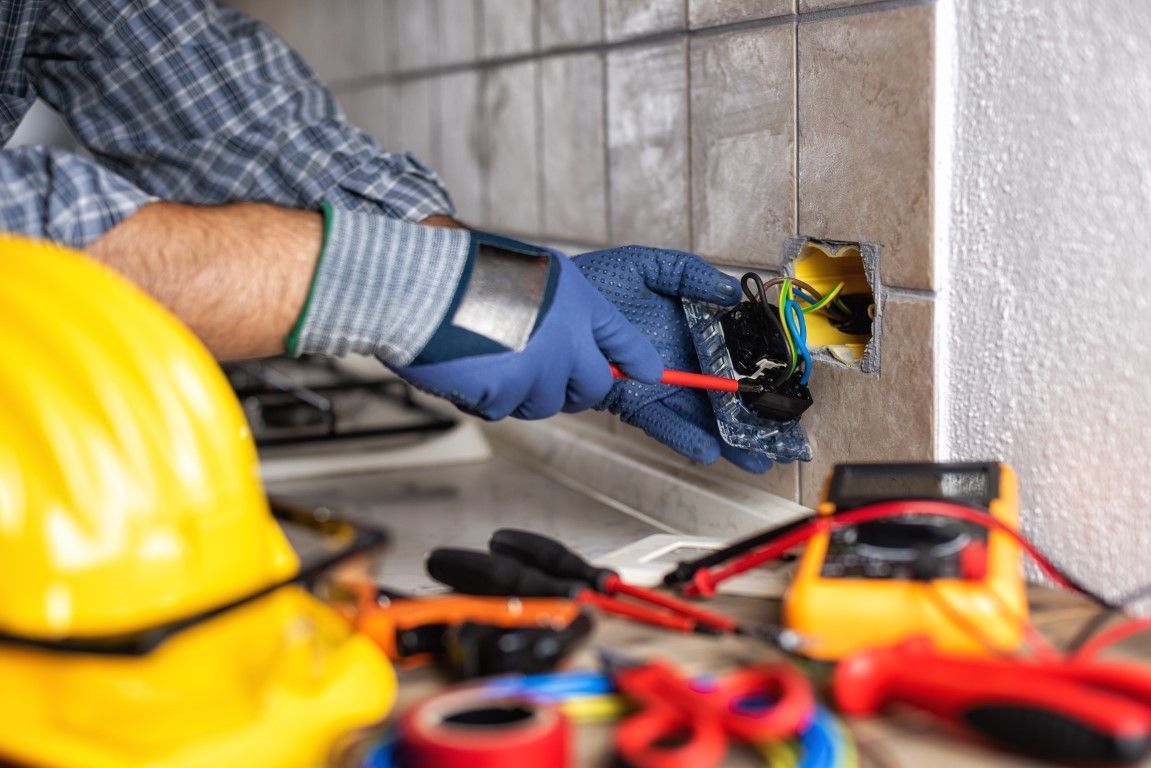 Electrician using a multimeter to test a wall outlet circuit.