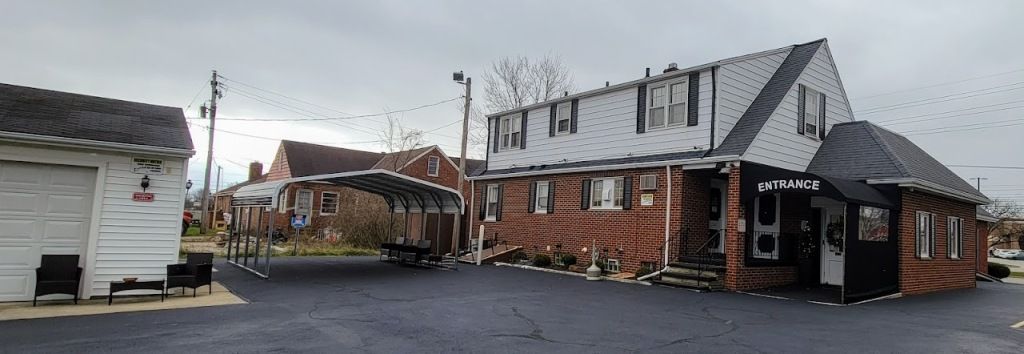 A brick building with a black awning and a parking lot on a cloudy day.