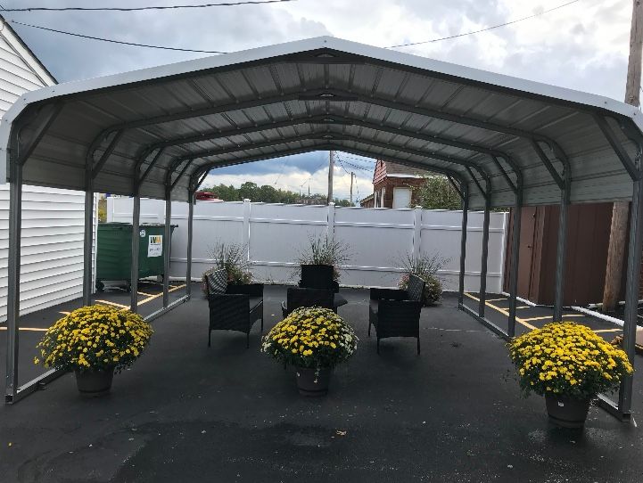 Metal carport with seating area: black chairs, flower pots, white fence. Gray sky.