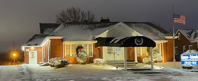 A snow-covered building with Christmas decorations and an American flag. Nighttime.