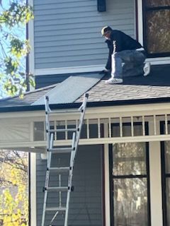 A man is kneeling on the roof of a house with a ladder.