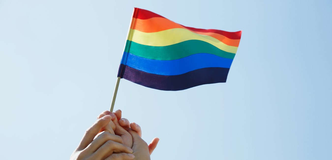 Hands holding a rainbow pride flag against a blue sky