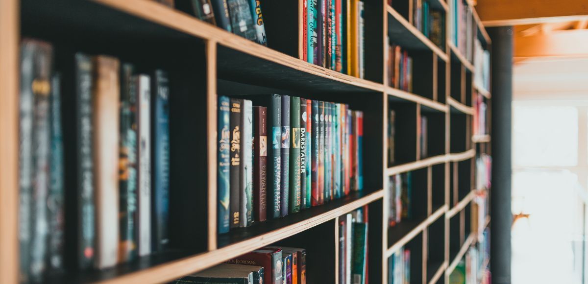 Bookshelves lined with colorful books in a narrow library aisle with bright light at the end