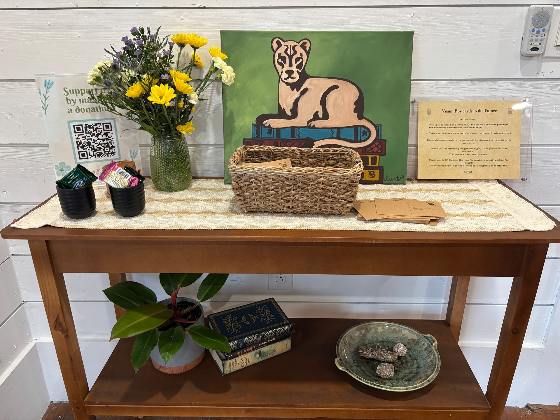 Wooden table with artwork, flowers, and books. Items include a lion painting, basket, and small plants.