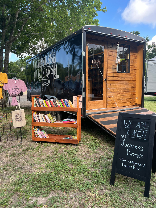 Mobile bookstore with wooden shelves, open door, and a chalkboard sign that reads, 