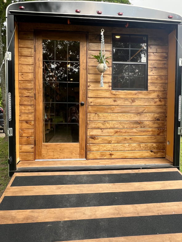 Exterior of a tiny house built into a black trailer with wooden siding and a glass door.