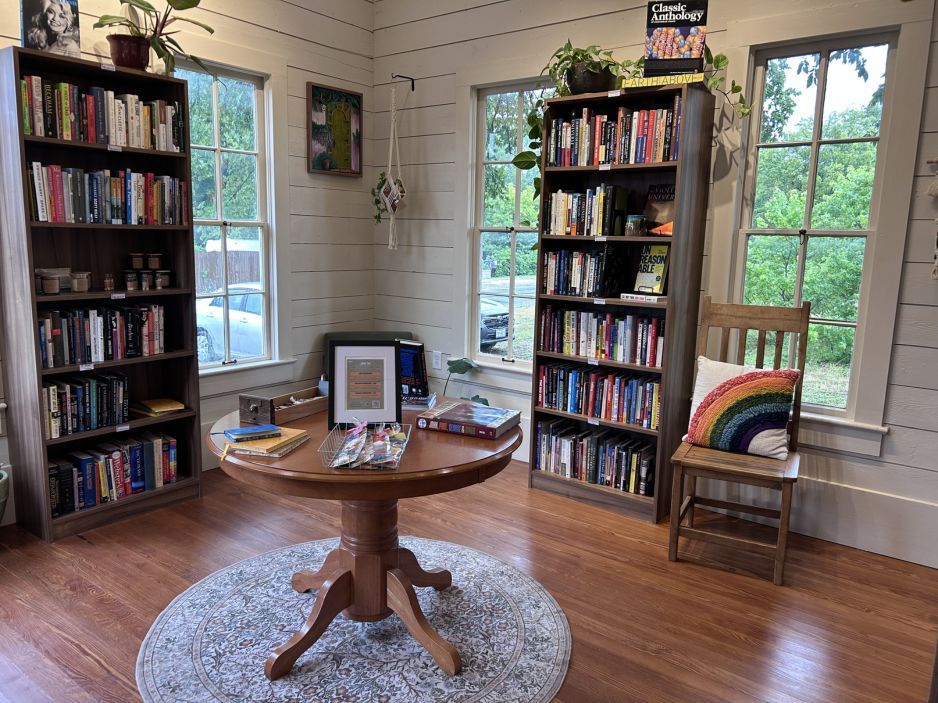 Cozy reading nook with bookshelves, a round table, chairs, windows, and a rug on wooden floors.