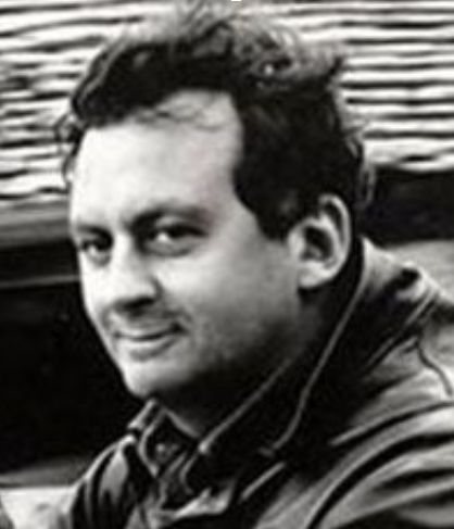 Man with dark hair smiling, wearing a jacket with a high collar.