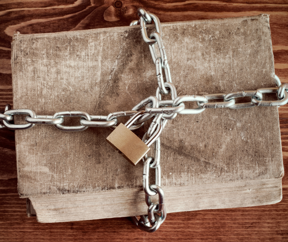 Old book bound by a chain and padlock on a wooden surface.