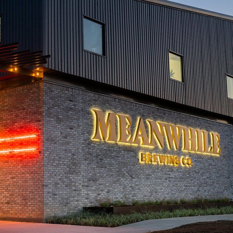 Illuminated brick building at night with a glowing red sign and large “MEANWHILE BREWING
