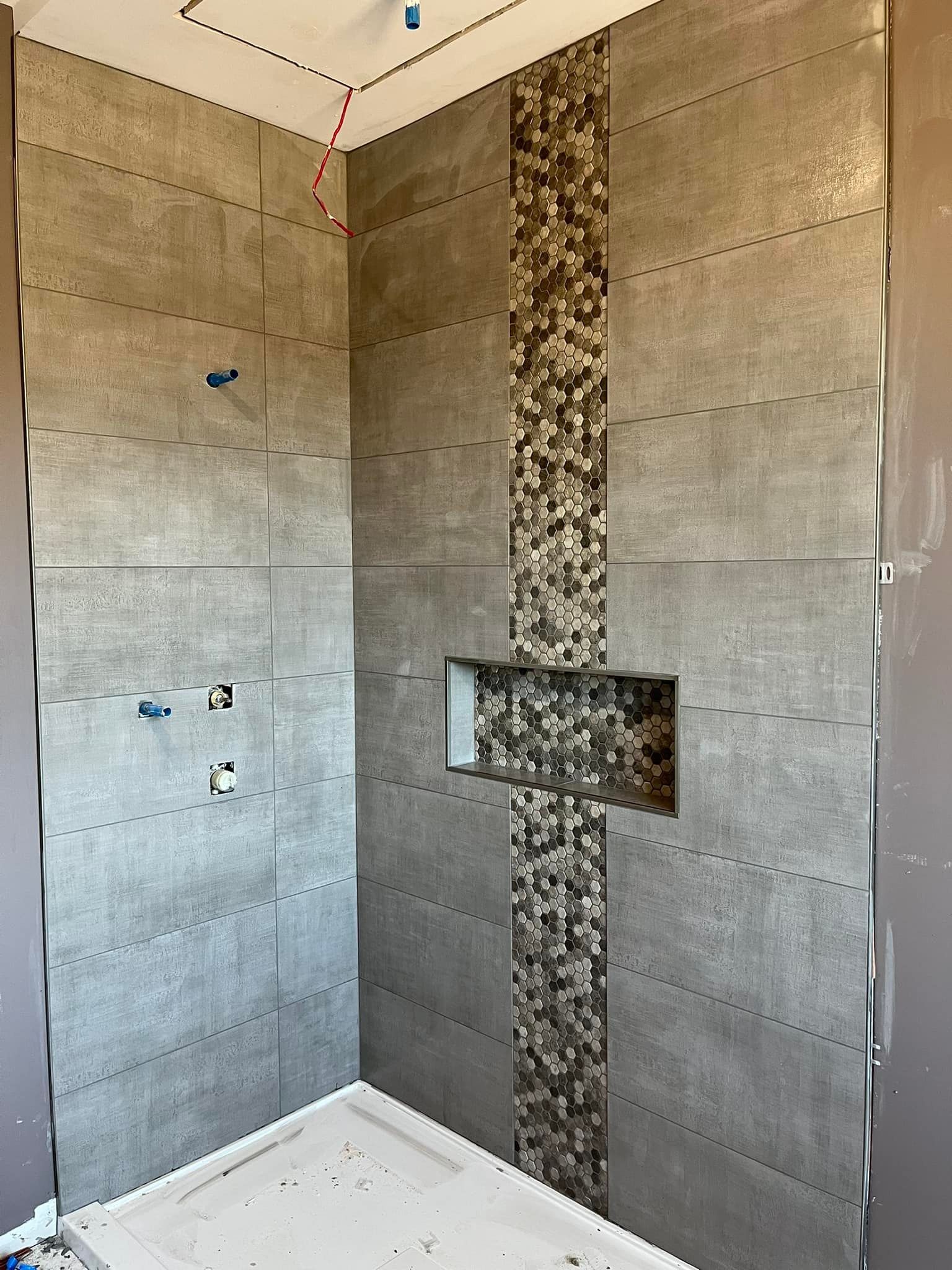 Une cabine de douche en construction avec des carreaux muraux rectangulaires gris, une frise centrale verticale en mosaïque et une niche.