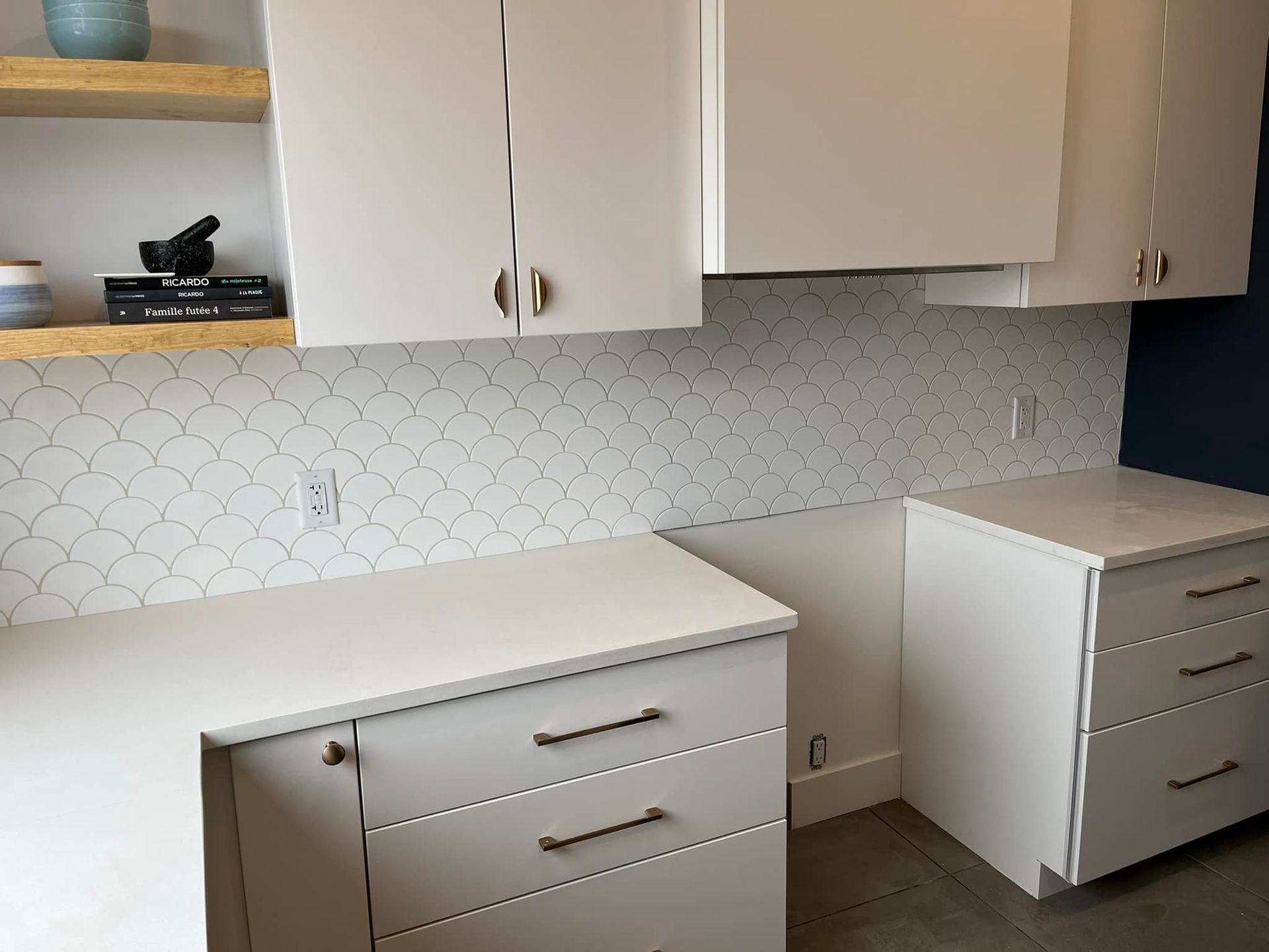 Armoires et tiroirs blancs avec poignées dorées, comptoirs en quartz et crédence en carrelage blanc à motif festonné.
