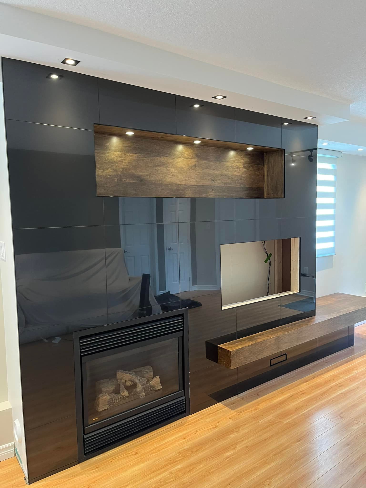 Un mur d'accent dans un salon moderne avec une cheminée, des étagères ouvertes, une niche pour la télévision, des panneaux noirs brillants et des touches de bois.