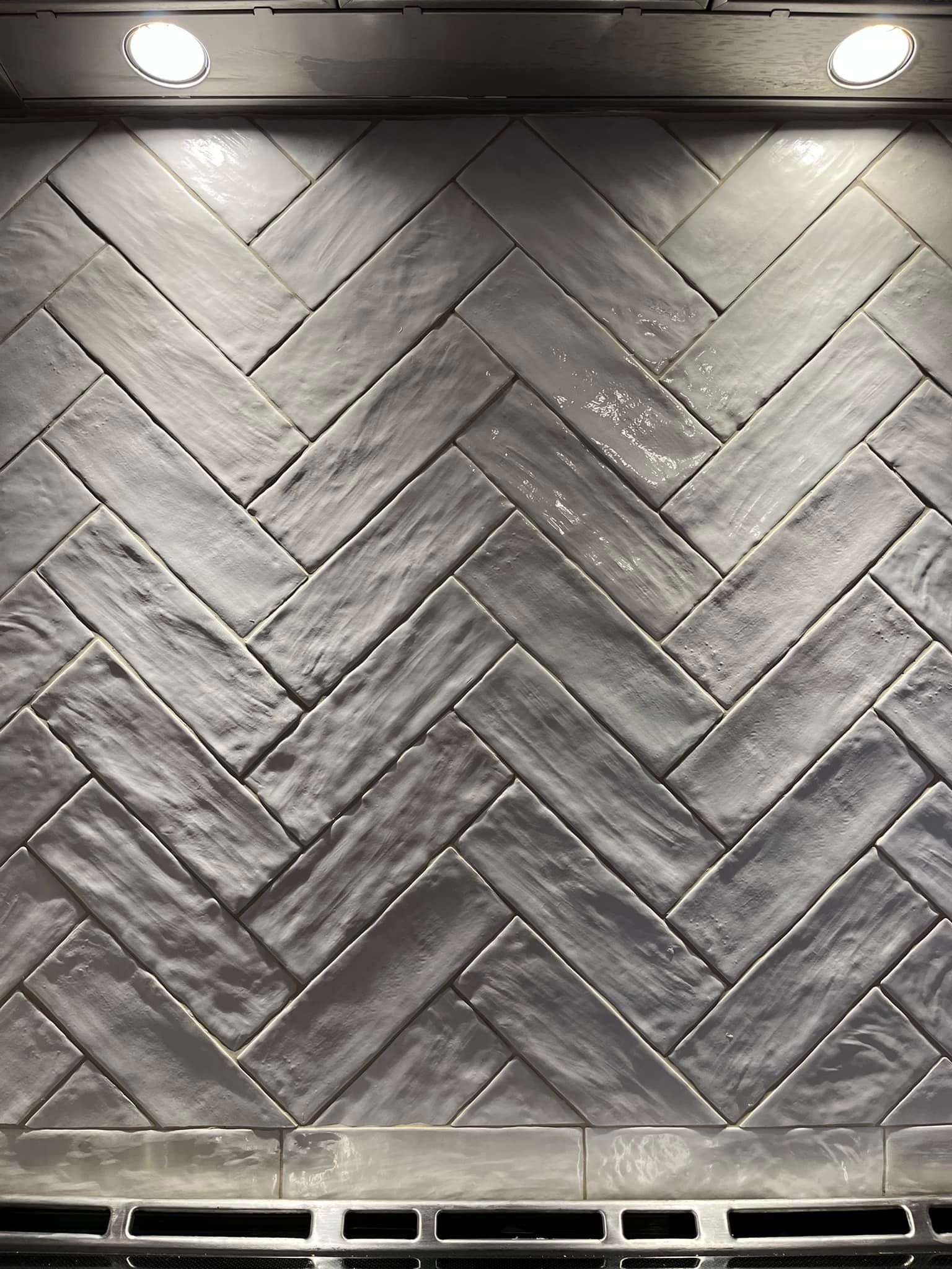 Gros plan sur une crédence de cuisine composée de carreaux rectangulaires gris texturés, posés en chevrons.