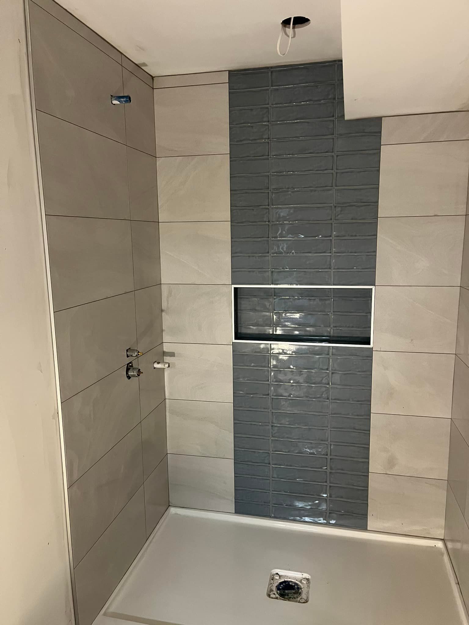 Une cabine de douche moderne avec de grands carreaux muraux beige clair et une bande verticale centrale de carreaux décoratifs texturés gris foncé.