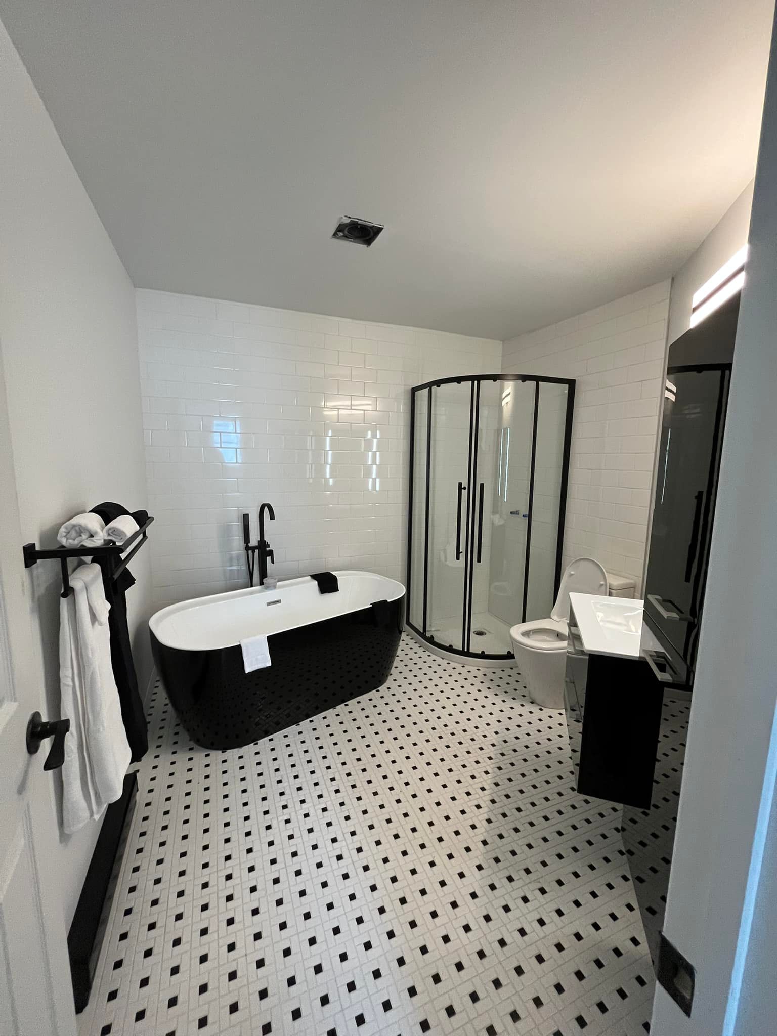 Une salle de bains moderne avec une baignoire îlot noire et blanche, une douche en verre incurvée et un carrelage au sol à motifs.
