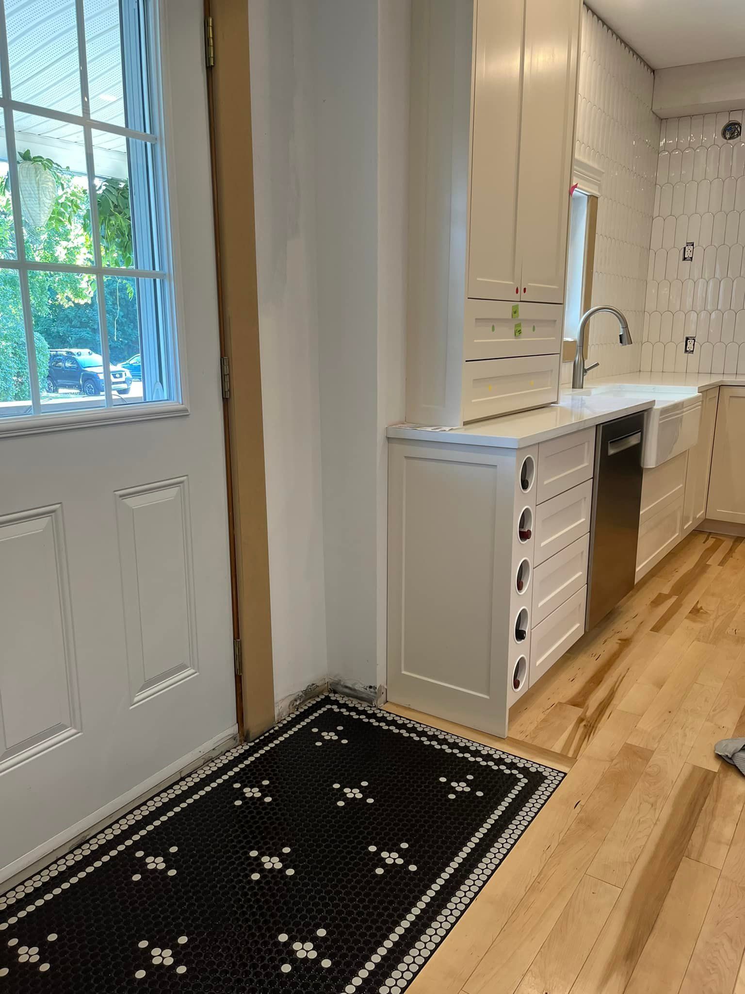 Une cuisine avec des armoires couleur crème, un lave-vaisselle en acier inoxydable, un parquet clair et un tapis noir à motifs.