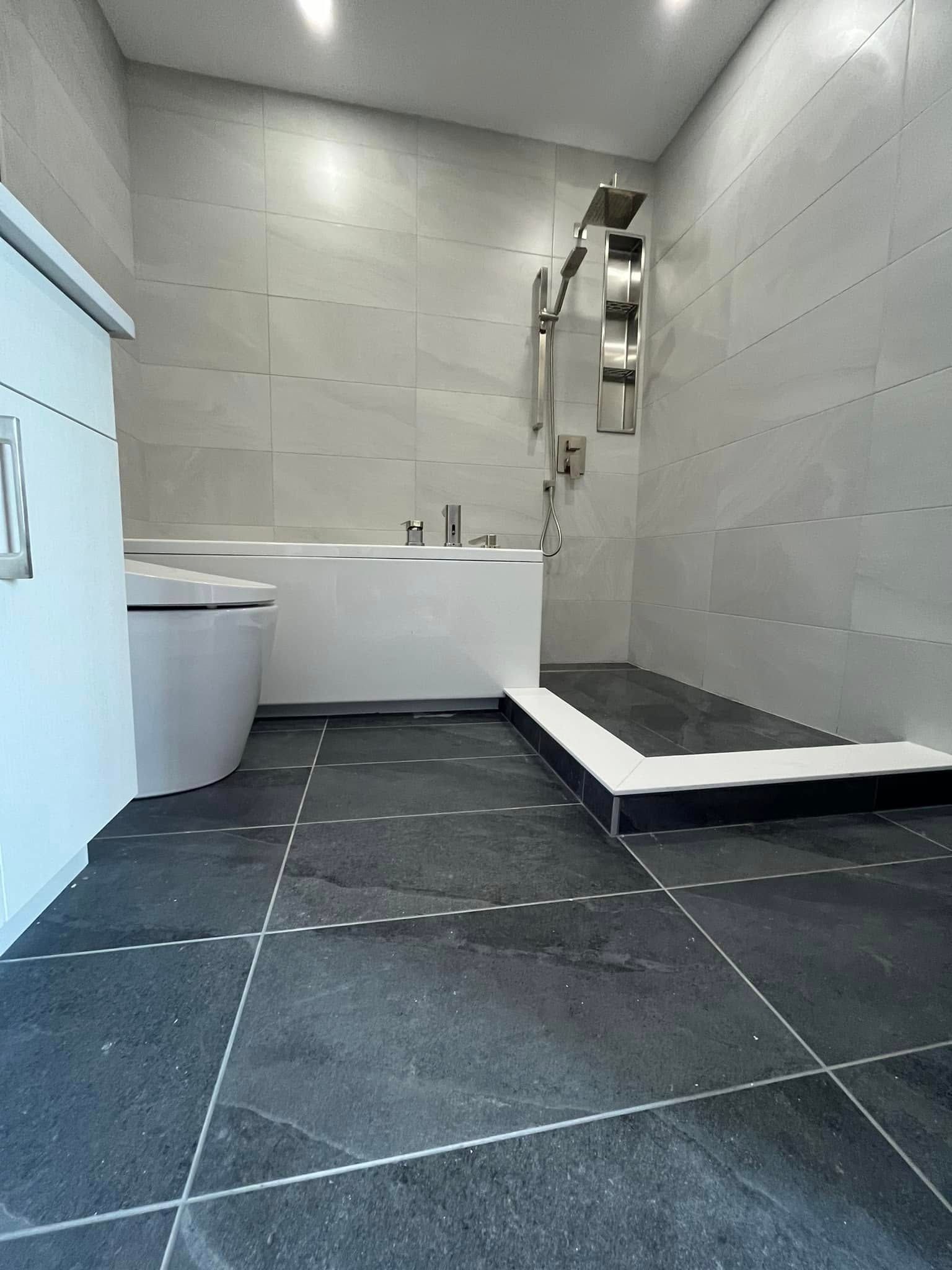 Modern bathroom with dark floor tiles, light wall tiles, a white toilet, and a raised walk-in shower area.