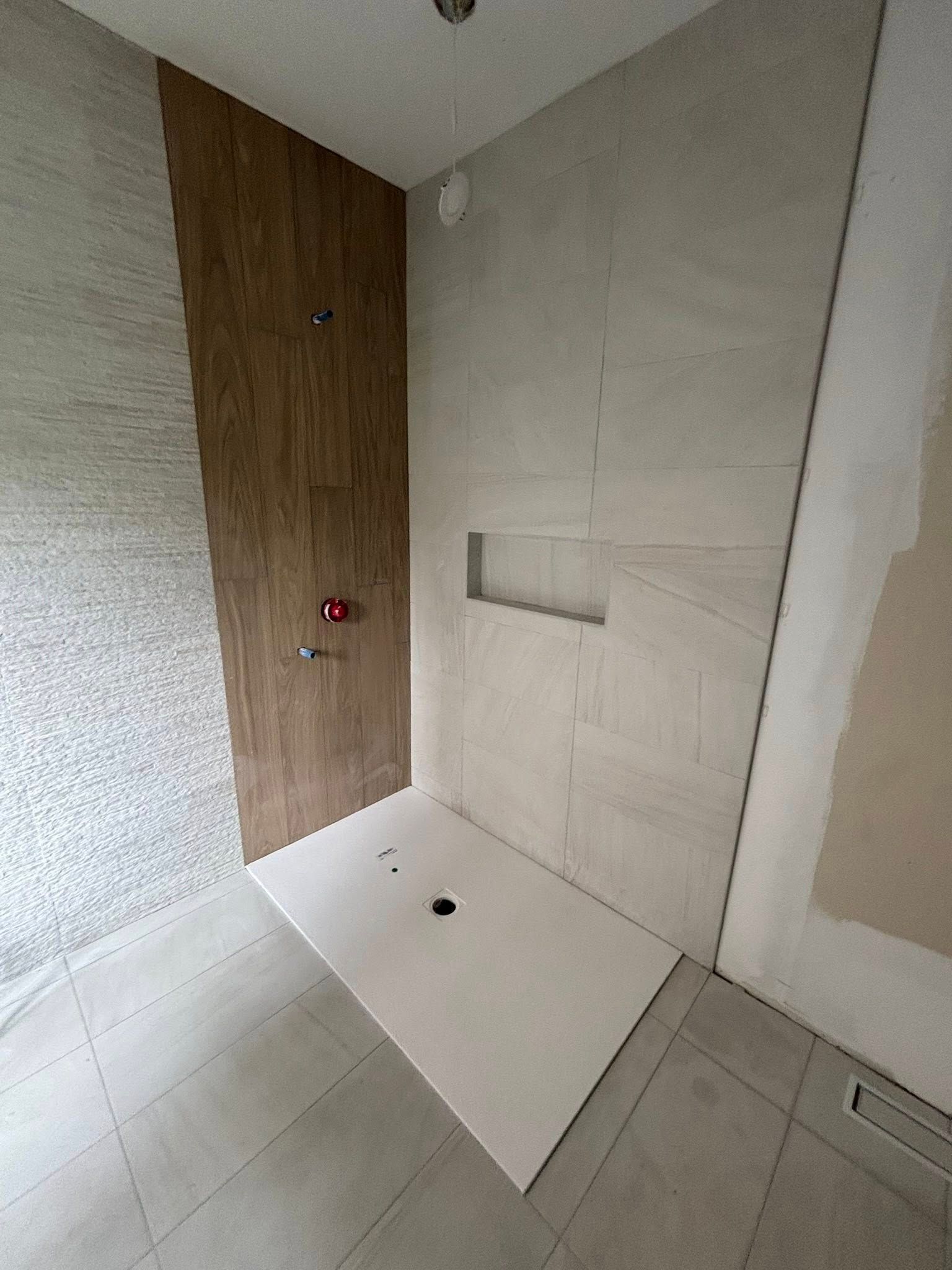 Une cabine de douche moderne avec carrelage imitation bois sur le mur de la plomberie, carrelage gris clair sur le mur du fond et receveur blanc.