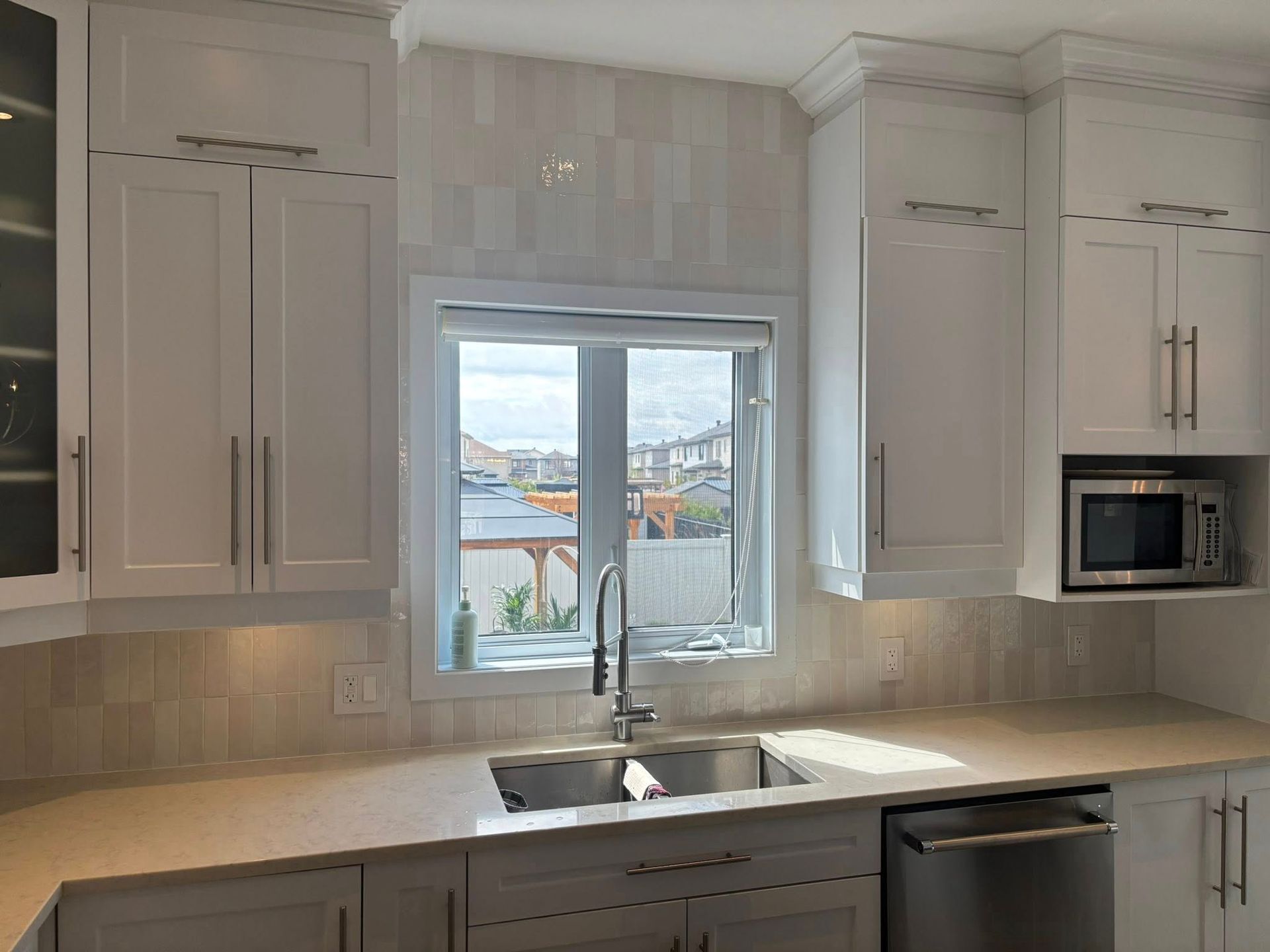 Cuisine moderne avec placards blancs de style shaker, évier en acier inoxydable avec robinet et micro-ondes intégré.