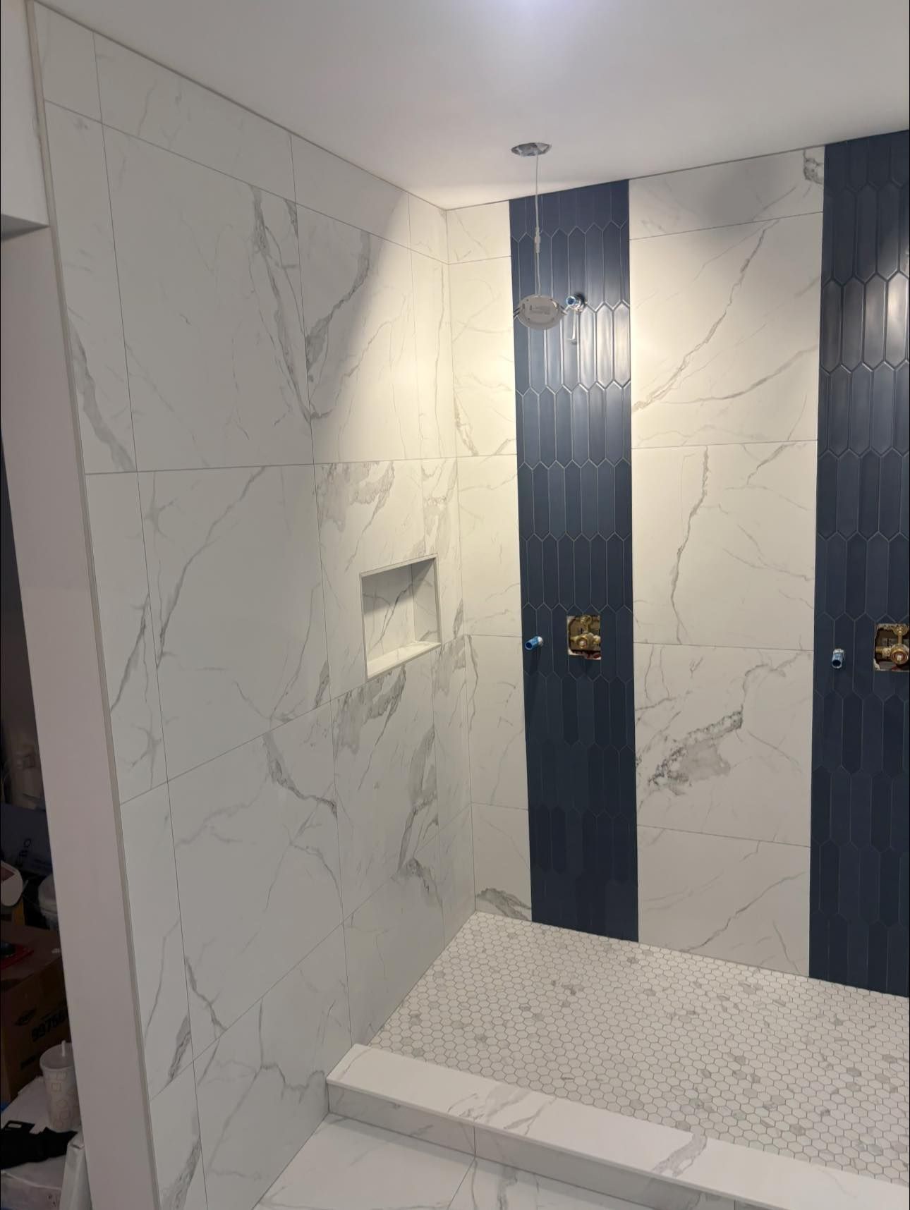 Une douche carrelée ornée de panneaux à motifs de marbre blanc contrastant avec deux bandes verticales de carreaux côtelés bleu marine.
