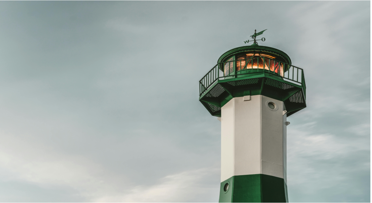 Green-and-white lighthouse against a cloudy sky, lit at the top